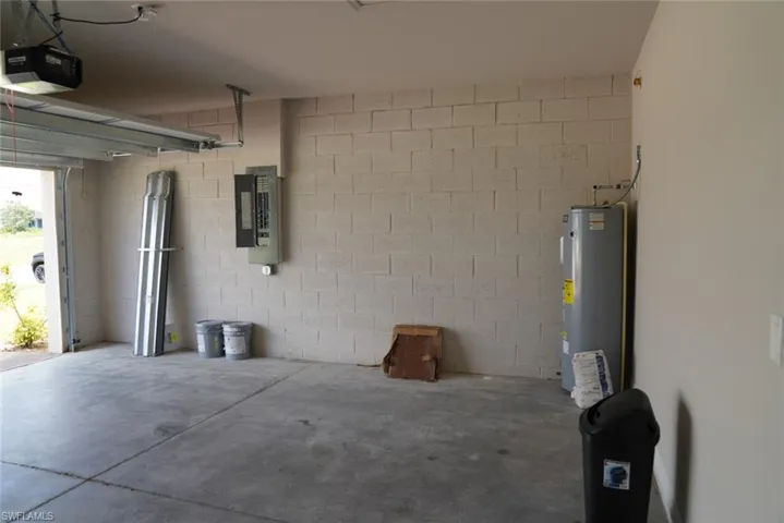 Garage featuring water heater, electric panel, concrete block wall, and a garage door opener