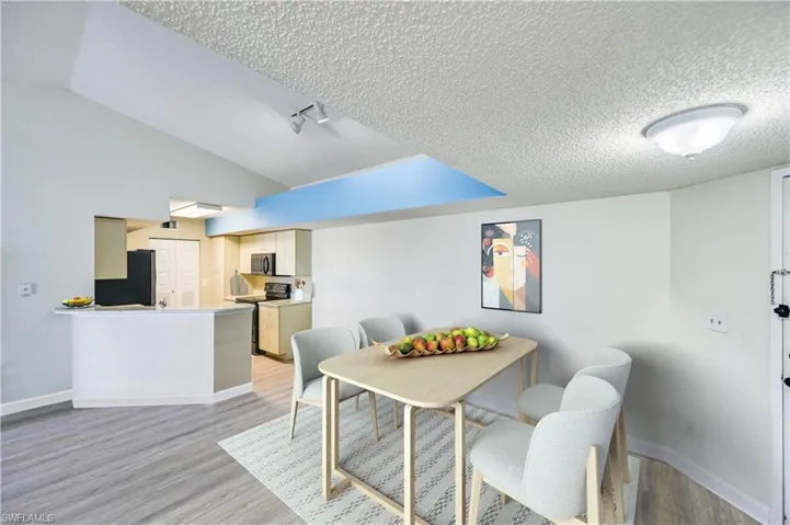 Dining area with a textured ceiling, light hardwood / wood-style flooring, lofted ceiling, and rail lighting