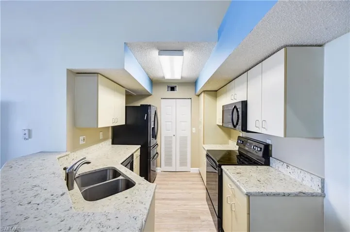 Kitchen with light hardwood / wood-style floors, stainless steel fridge, black / electric stove, sink, and a textured ceiling