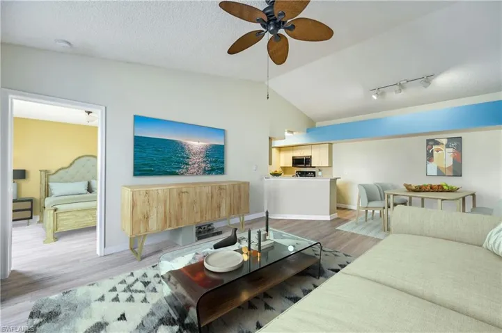 Living room featuring ceiling fan, vaulted ceiling, a textured ceiling, rail lighting, and light hardwood / wood-style floors