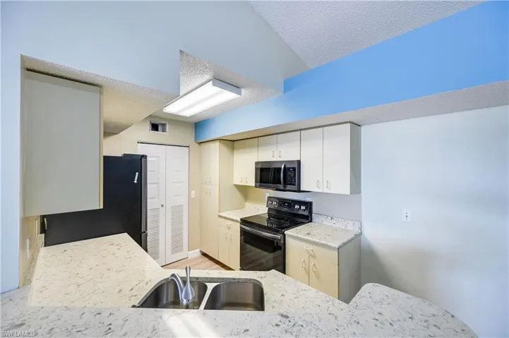 Kitchen featuring light wood-type flooring, fridge, sink, black range with electric cooktop, and white cabinets