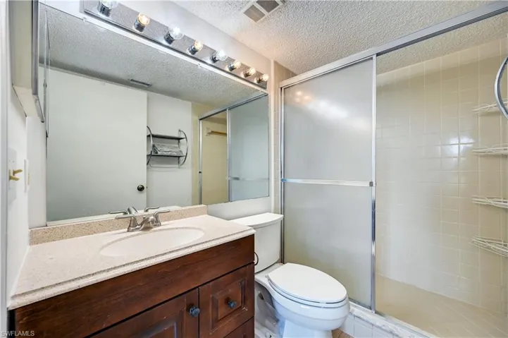 Bathroom featuring vanity, a shower with door, toilet, and a textured ceiling