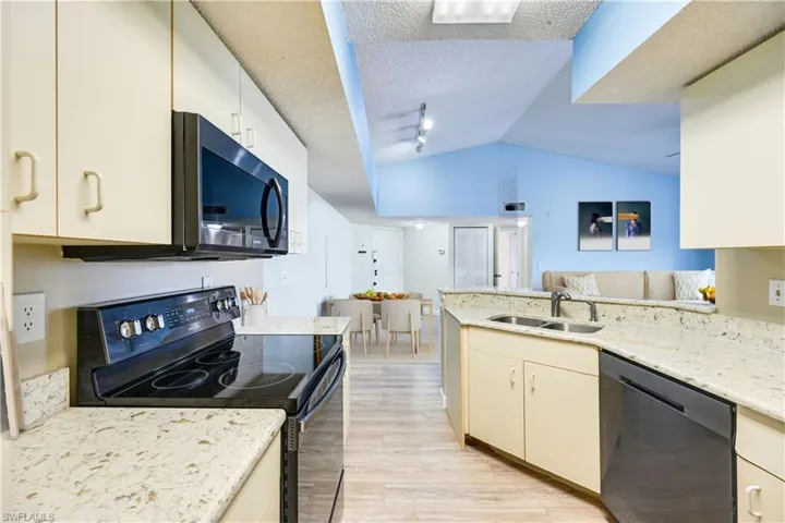 Kitchen with lofted ceiling, black appliances, sink, light hardwood / wood-style floors, and a textured ceiling