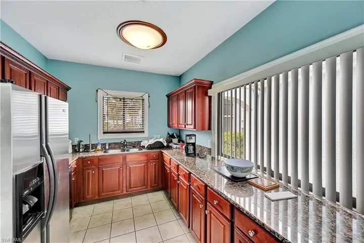 Kitchen featuring light stone counters, stainless steel refrigerator with ice dispenser, sink, and light tile patterned flooring