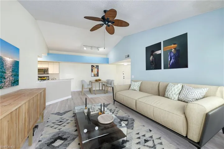 Living room with ceiling fan, vaulted ceiling, light hardwood / wood-style flooring, track lighting, and a textured ceiling