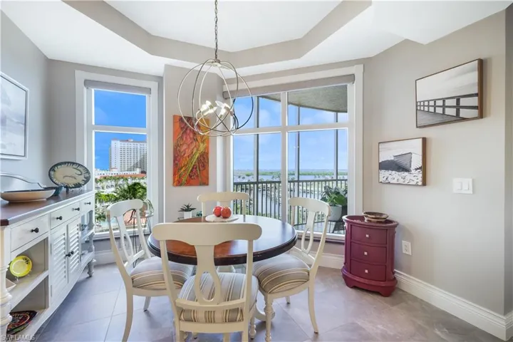 Dining room featuring a tray ceiling, a chandelier, light tile patterned flooring, and a water view