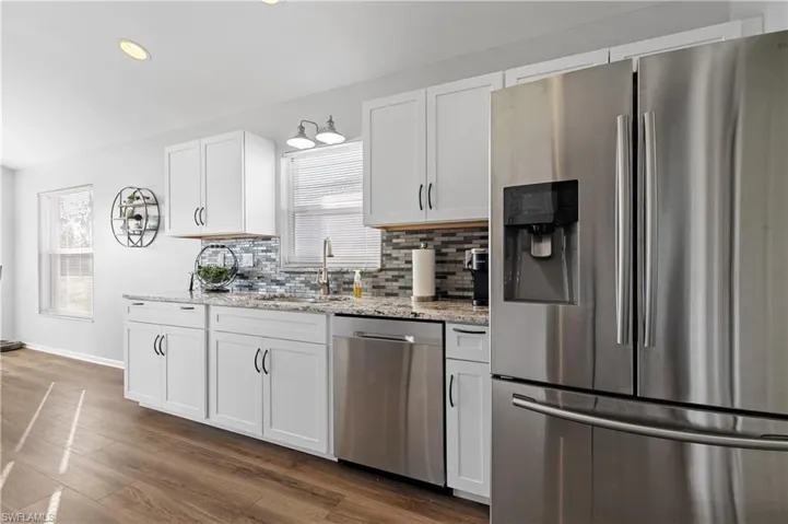 Kitchen featuring sink, appliances with stainless steel finishes, light stone counters, tasteful backsplash, and white cabinets
