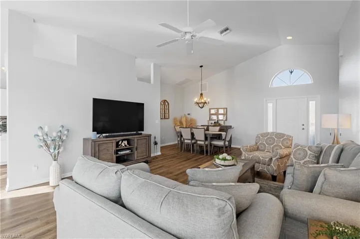 Living room with ceiling fan with notable chandelier, high vaulted ceiling, and hardwood / wood-style floors