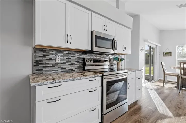 Kitchen with appliances with stainless steel finishes, white cabinetry, wood-type flooring, decorative backsplash, and light stone countertops