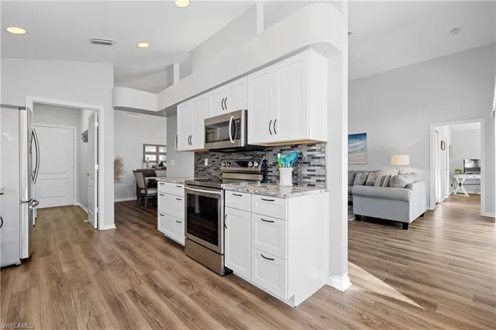 Kitchen with white cabinetry, high vaulted ceiling, stainless steel appliances, tasteful backsplash, and light stone countertops