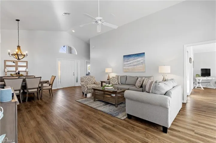 Living room featuring wood-type flooring, ceiling fan with notable chandelier, and high vaulted ceiling
