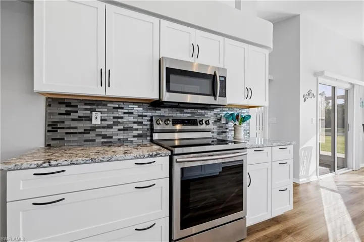 Kitchen with stainless steel appliances, white cabinetry, light stone countertops, and decorative backsplash