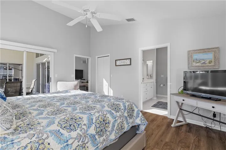 Bedroom featuring dark wood-type flooring, ensuite bathroom, high vaulted ceiling, ceiling fan, and access to exterior
