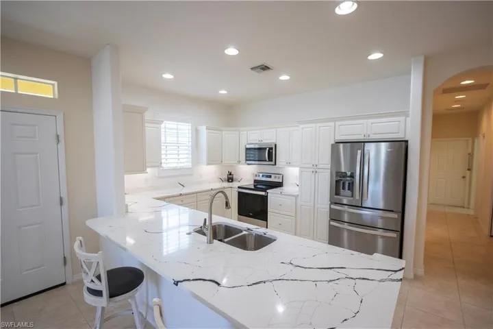 Kitchen featuring a large island with sink, white shaker-style cabinetry, stainless steel appliances, recessed lighting, and a transom window