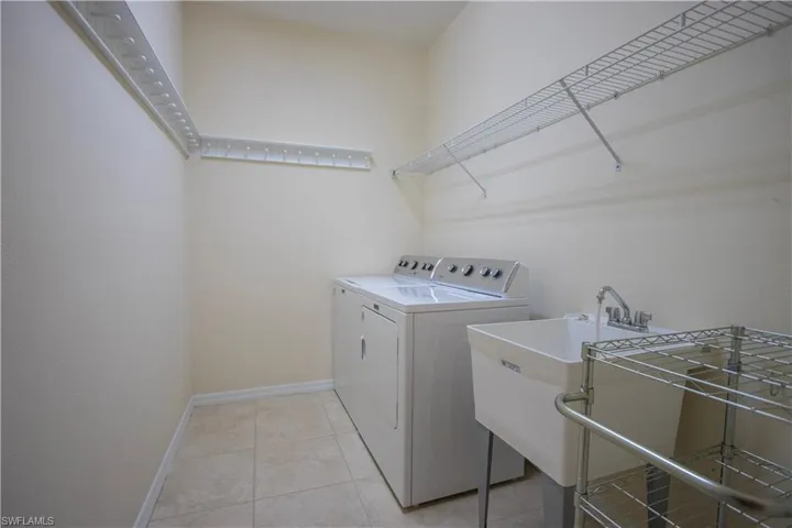 Laundry area featuring tile flooring, a utility sink with a chrome faucet, and ample wire shelving
