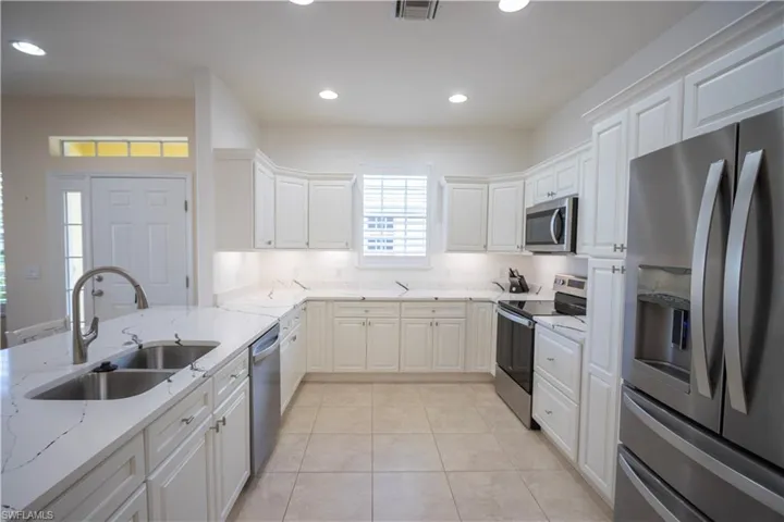 Well-appointed kitchen featuring white cabinetry, stainless steel appliances, a double basin sink, stone countertops, and recessed lighting
