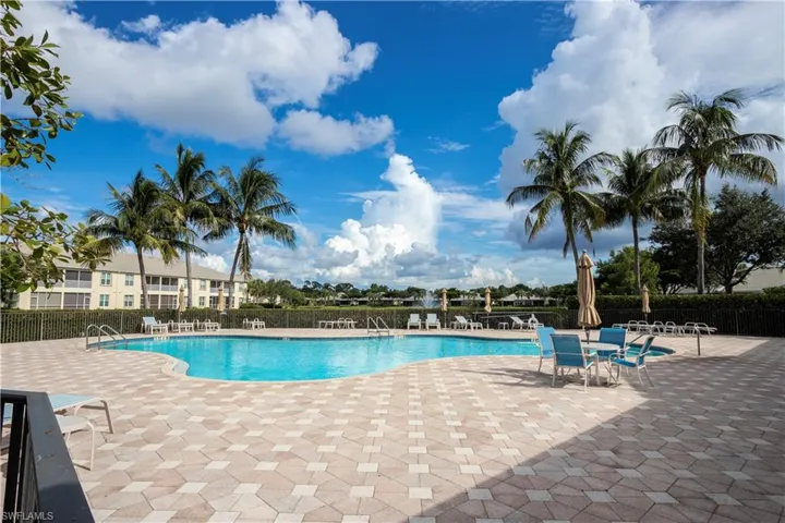 Expansive pool deck with patterned pavers, large swimming pool, and multiple palm trees