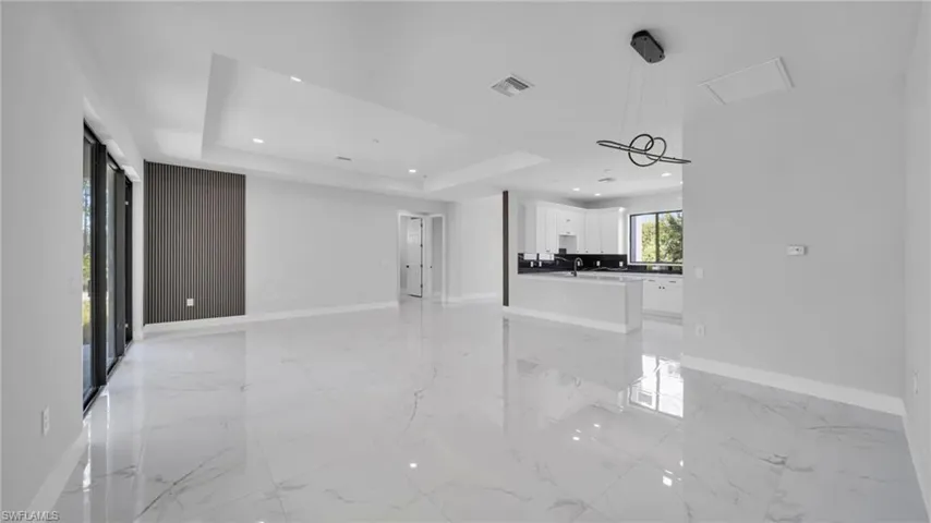 Unfurnished living room featuring recessed lighting, light marble finish flooring, and a tray ceiling