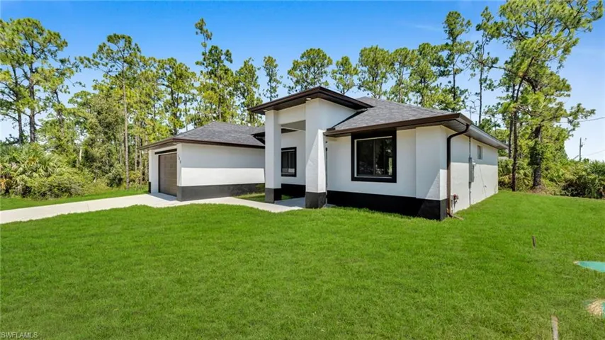 View of front facade featuring concrete driveway, roof with shingles, a front lawn, and a garage
