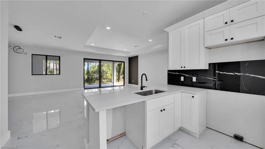 Kitchen with light marble finish flooring, open floor plan, a raised ceiling, a peninsula, and white cabinets