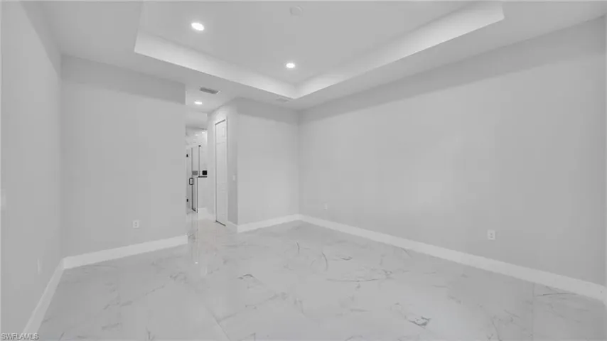 Unfurnished room with a tray ceiling, light marble finish flooring, and recessed lighting