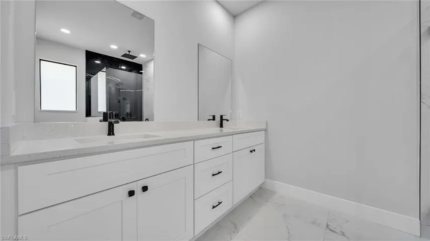 Full bath featuring double vanity, marble look tile flooring, a shower stall, and recessed lighting