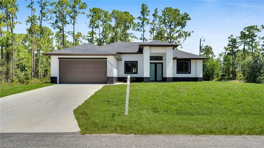 Prairie-style home with driveway, a garage, a shingled roof, stucco siding, and a front lawn