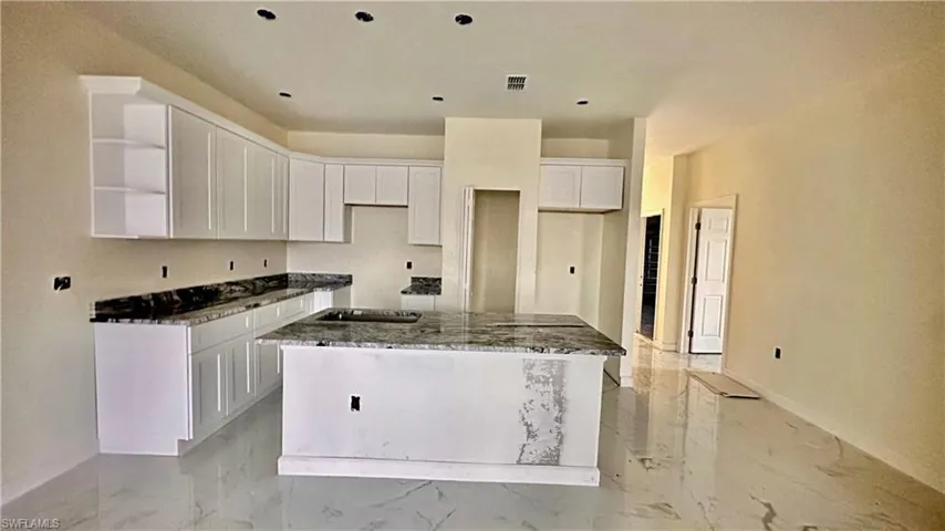 Kitchen with white cabinets, dark stone counters, and a kitchen island