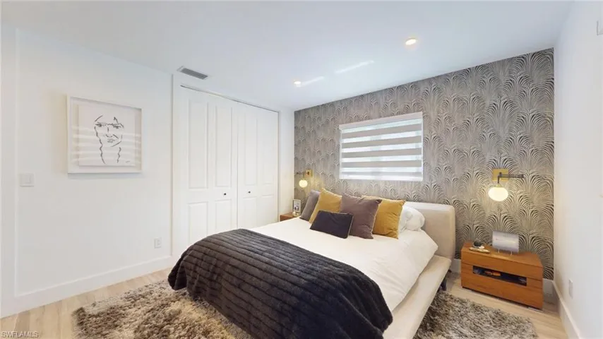 Bedroom with wood finished floors, visible vents, baseboards, and an accent wall