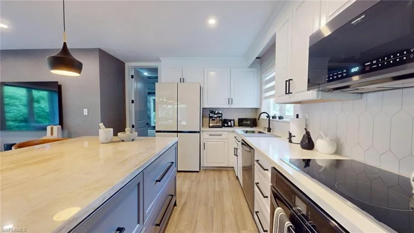 Kitchen featuring light wood-style flooring, stainless steel appliances, white cabinets, light countertops, and decorative backsplash