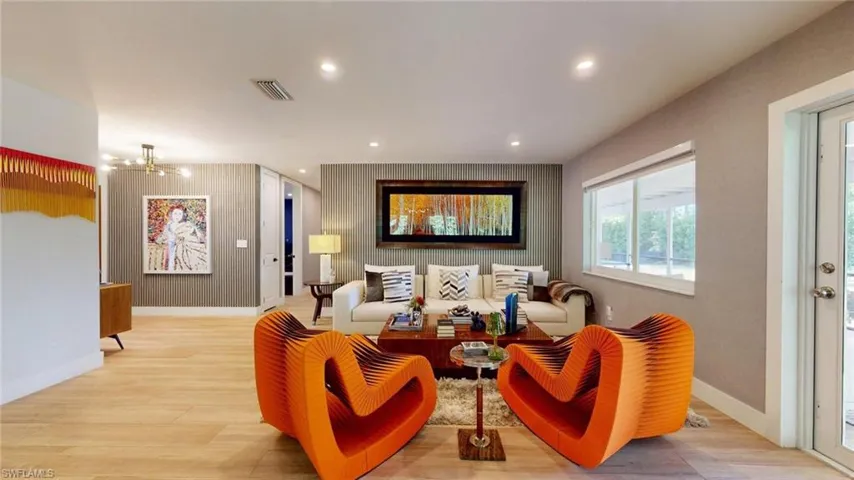 Living area featuring light wood-type flooring, visible vents, baseboards, and a notable chandelier