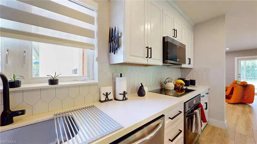 Kitchen with black electric cooktop, oven, tasteful backsplash, and white cabinets