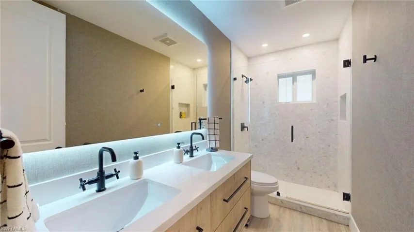 Bathroom featuring a sink, toilet, a stall shower, and wood finished floors