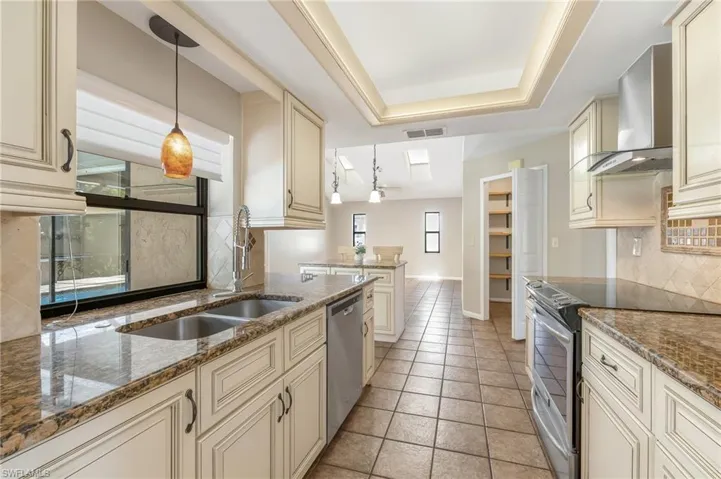 Kitchen featuring light-toned cabinetry, granite countertops, stainless steel appliances, and a tiled backsplash. Pass-thru to lanai area.