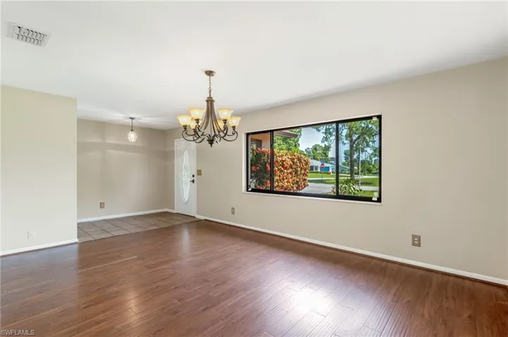 Spacious front  living area featuring ample natural light, wood-finish flooring, a decorative chandelier and picture window.