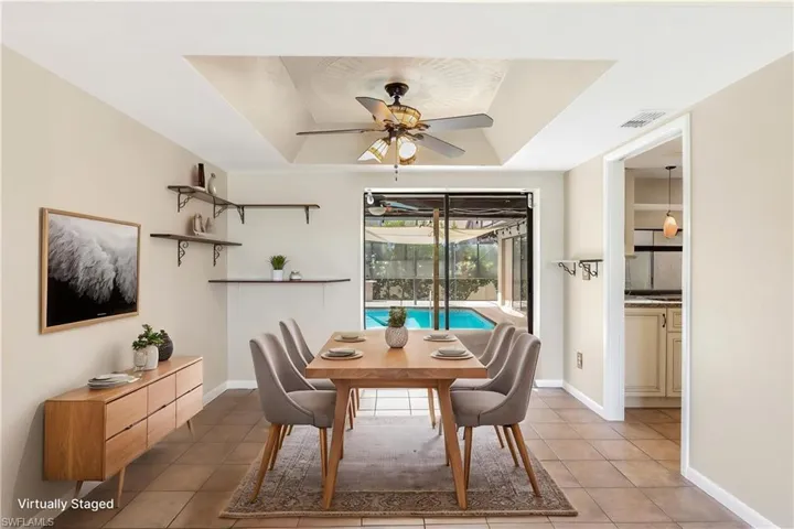 Virtually Staged - Dining area featuring a tray ceiling with a ceiling fan, tile flooring, and direct access to an outdoor pool area