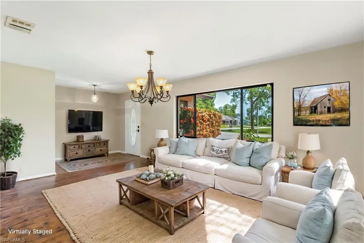 Virtually Staged - Spacious living area featuring ample natural light, wood-finish flooring, and a decorative chandelier