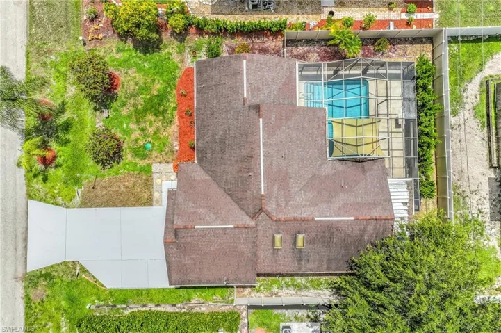 Property featuring a paved driveway, a large shingled roof, a screened-in swimming pool, and a private fenced yard with mature landscaping