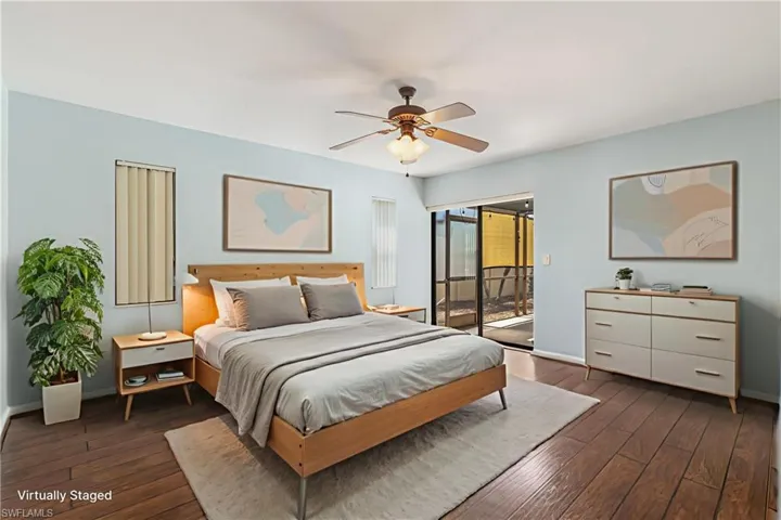 Virtually Staged Wood-finish flooring throughout, featuring a ceiling fan with integrated lighting, sliding glass doors to an outdoor area, and vertical blinds