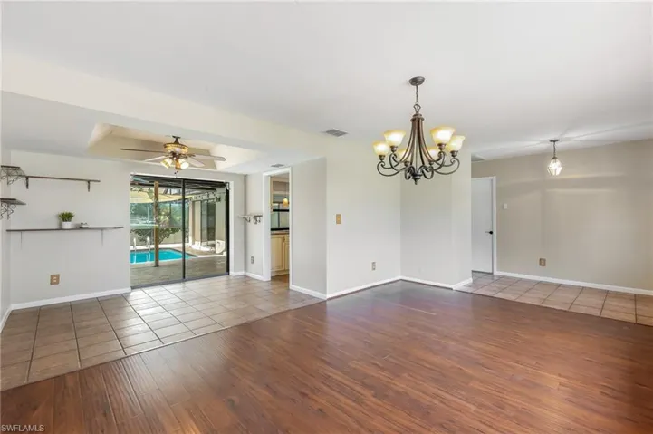 Combined dining and living areas with wood-finish flooring, a contemporary chandelier, and direct access to a screened-in pool patio.