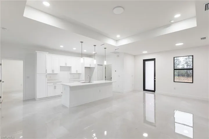 Kitchen with sink, white cabinetry, a tray ceiling, pendant lighting, and a kitchen island with sink