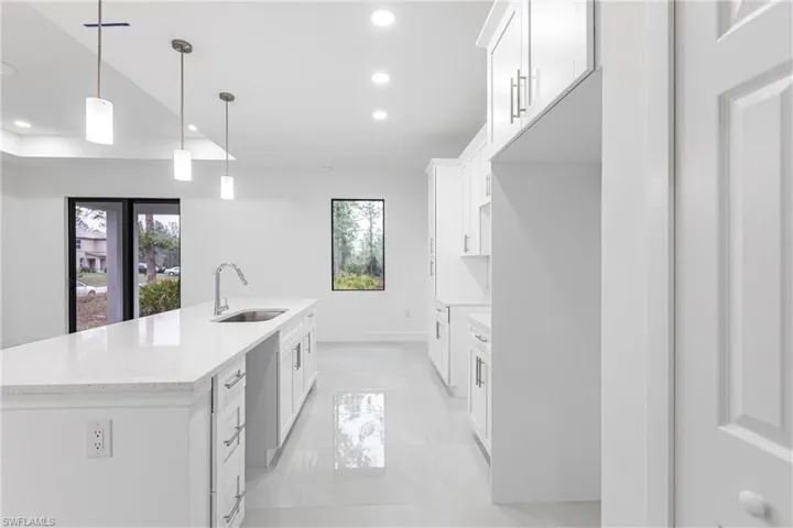 Kitchen featuring white cabinetry, sink, decorative light fixtures, and a kitchen island with sink