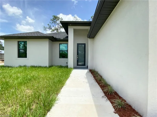 Property entrance featuring stucco siding, a shingled roof, and a lawn