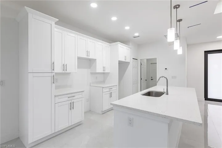 Kitchen with white cabinetry, pendant lighting, sink, and a center island with sink