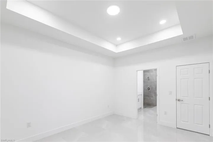 Unfurnished bedroom featuring a tray ceiling and ensuite bath