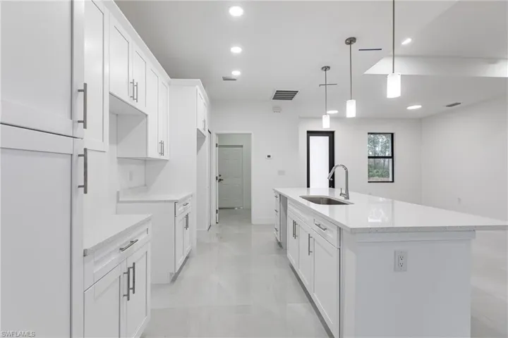 Kitchen featuring white cabinetry, an island with sink, sink, hanging light fixtures, and light stone counters