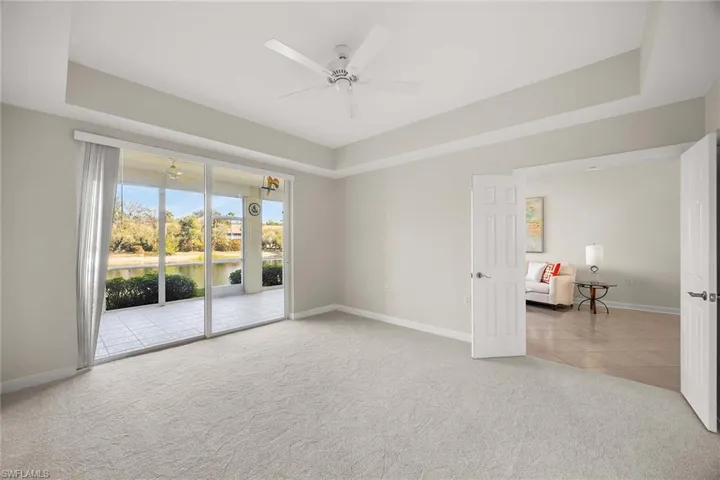 Unfurnished room with a tray ceiling, light carpet, ceiling fan, and a water view