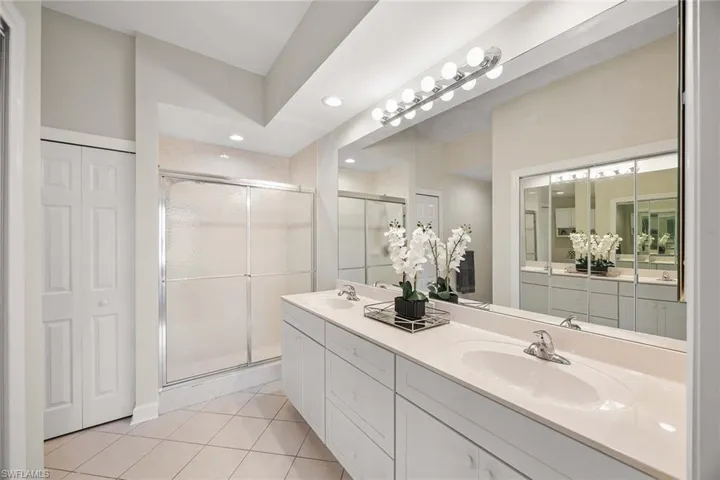 Bathroom with double vanity, a stall shower, light tile patterned floors, and a closet