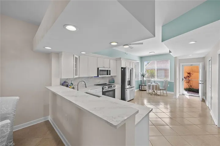 Kitchen featuring a peninsula, stainless steel appliances, decorative backsplash, glass insert cabinets, and light tile patterned floors