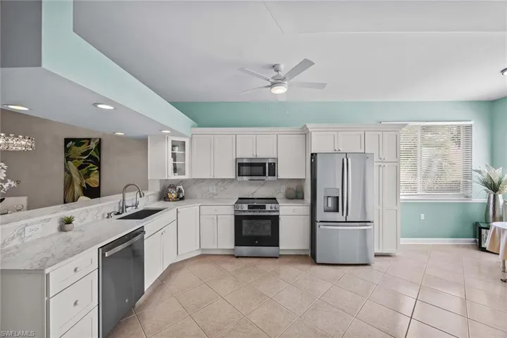 Kitchen with stainless steel appliances, ceiling fan, white cabinets, glass fronted cabinets, and backsplash